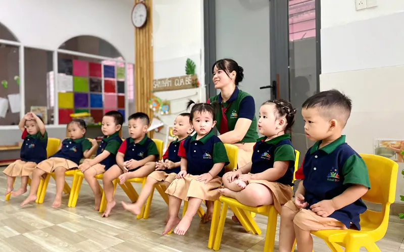 Các bé ngồi ghế nhỏ quanh cô trong lớp buổi sáng